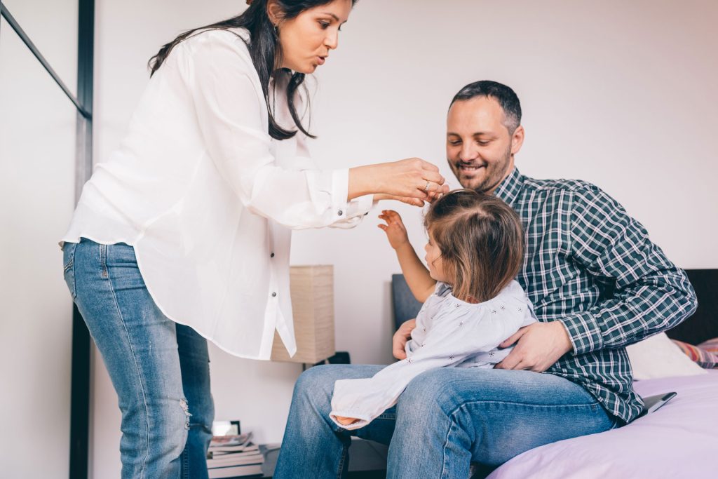 Parents helping their daughter wear a hair clip.