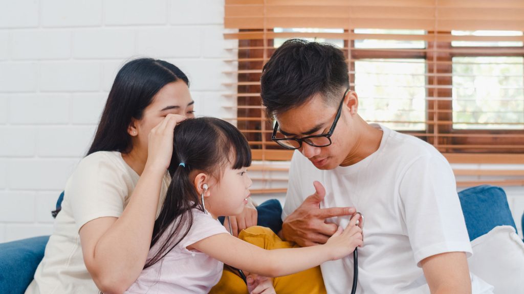 Asian parents playing doctor with their daughter.