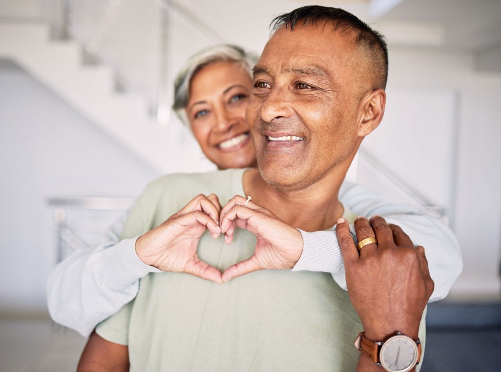 Wife hugging his husband and creating a heart shape with her hands.