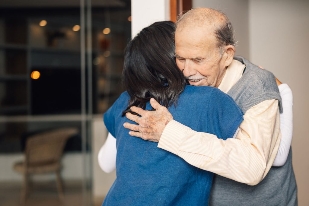 Elderly man embracing a nurse visiting him at home.